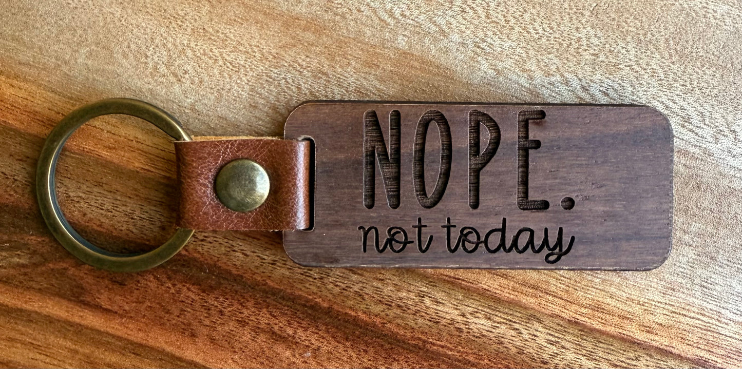 Wooden keychain with leather strap and 'NOPE. not today' text on a wooden surface