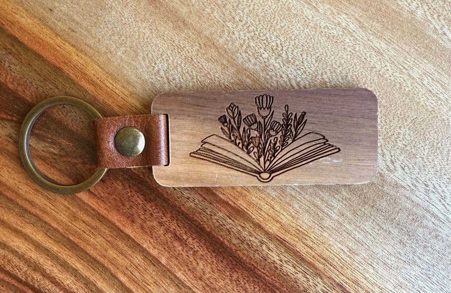 Wooden keychain with leather strap and engraved design on a wooden surface
