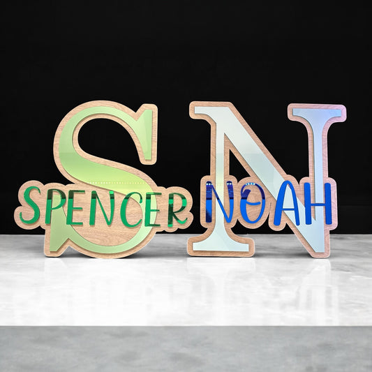 Wooden letters spelling 'SPENCER NOAH' on a white surface with a black background