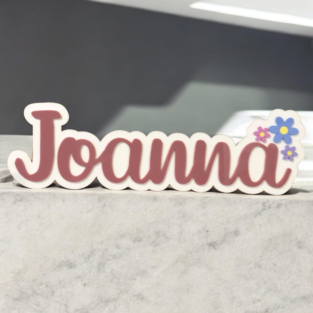 Decorative nameplate with 'Joanna' and floral designs on a marble surface