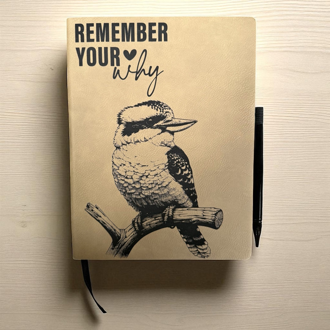 Notebook with a bird illustration and 'Remember Your Why' text on a wooden surface