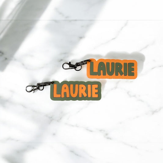 Two keychains with 'Laurie' on them against a marble background