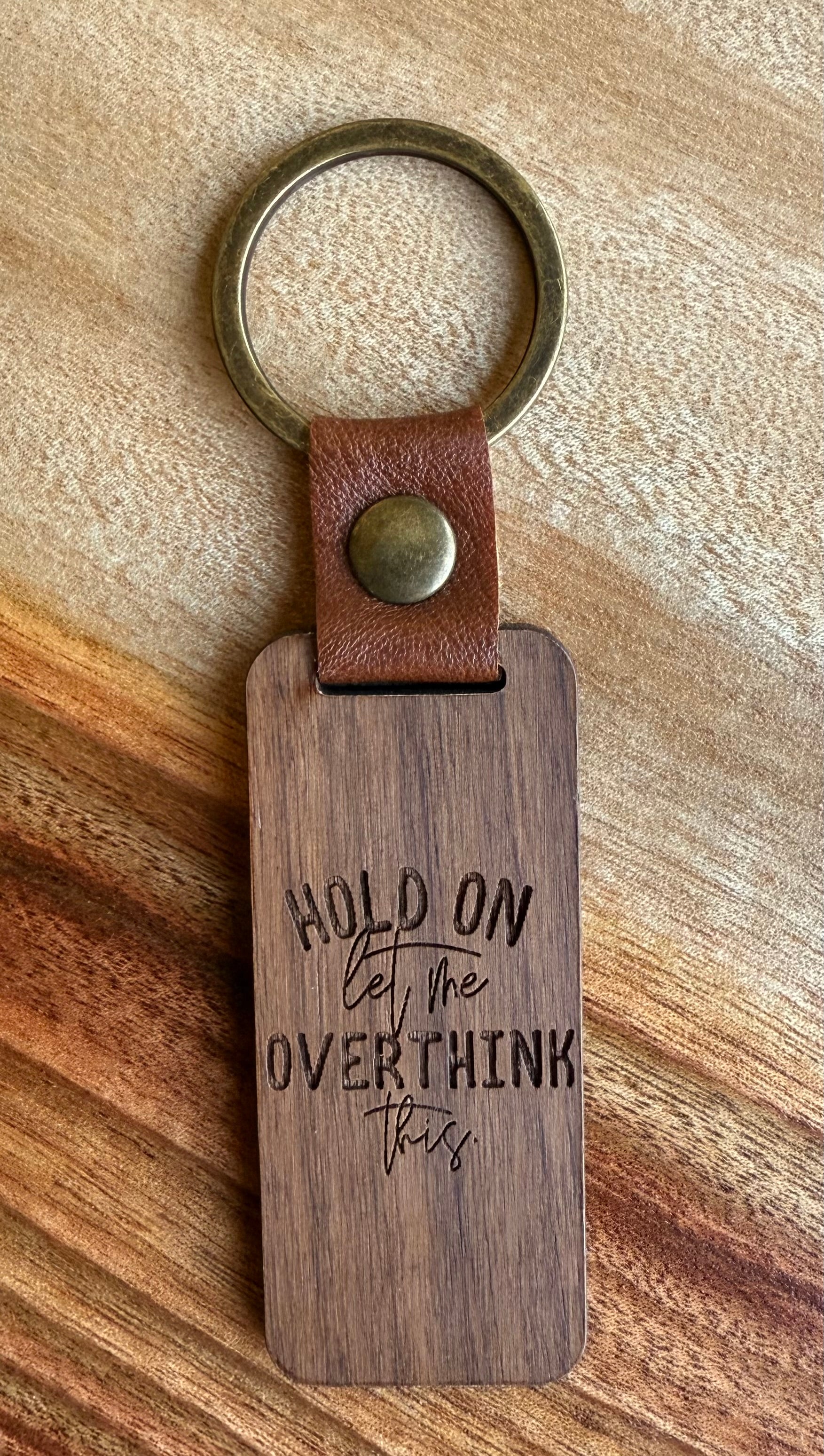 Wooden keychain with leather strap and engraved text on a wooden surface