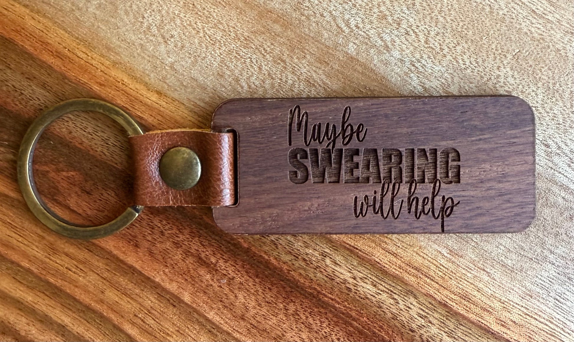Wooden keychain with leather strap and engraved text on a wooden surface