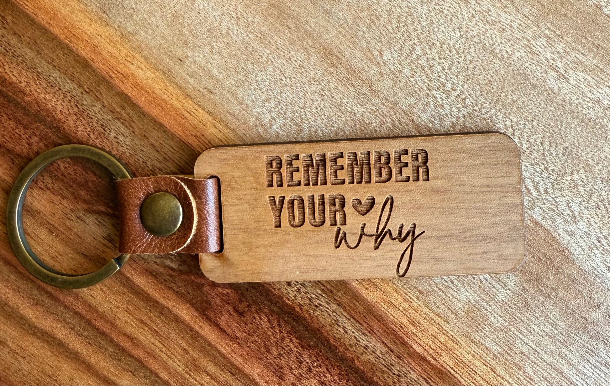 Wooden keychain with leather strap and engraved text on a wooden surface