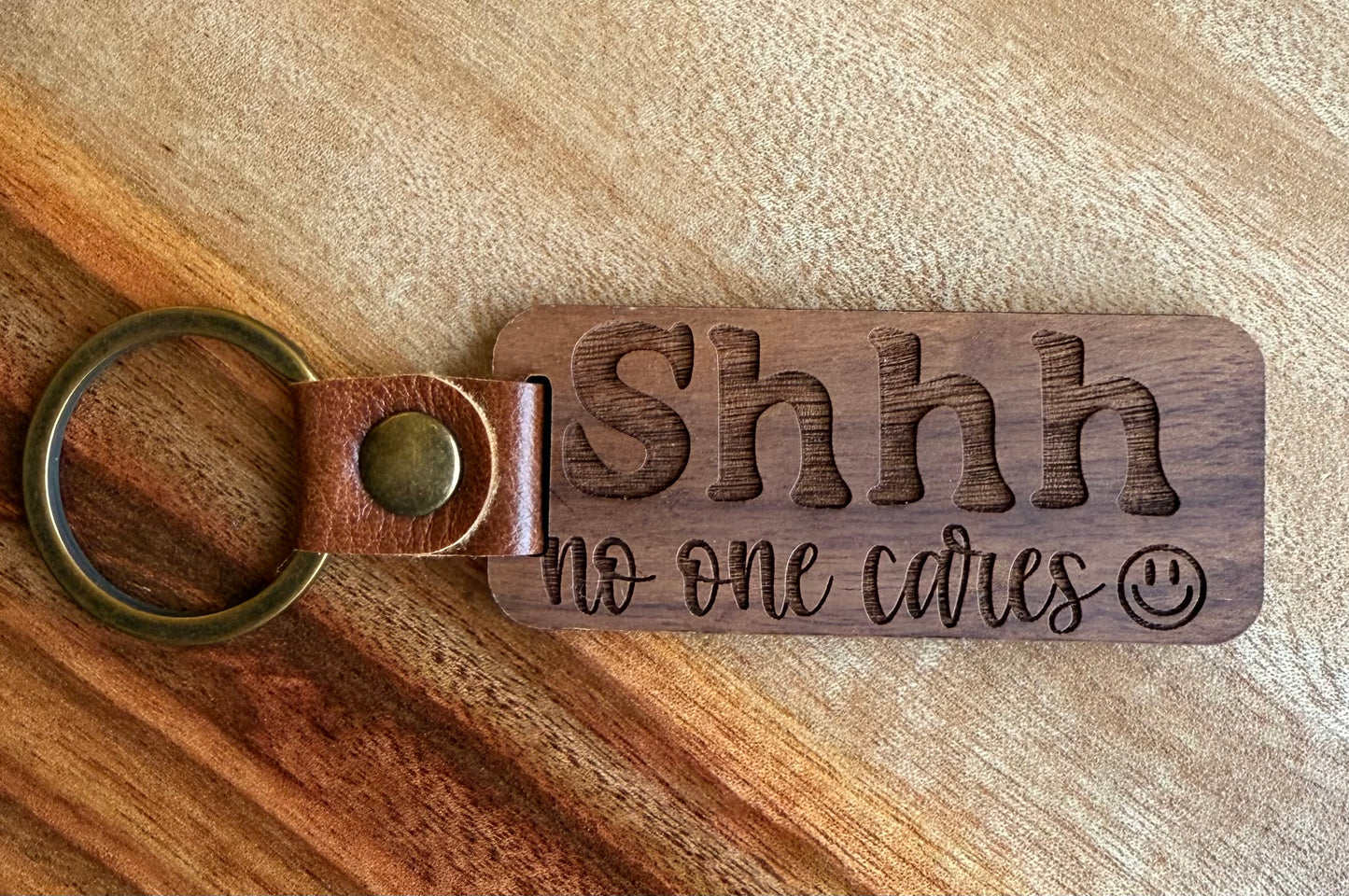 Wooden keychain with 'Shhh no one cares' text on a wooden surface