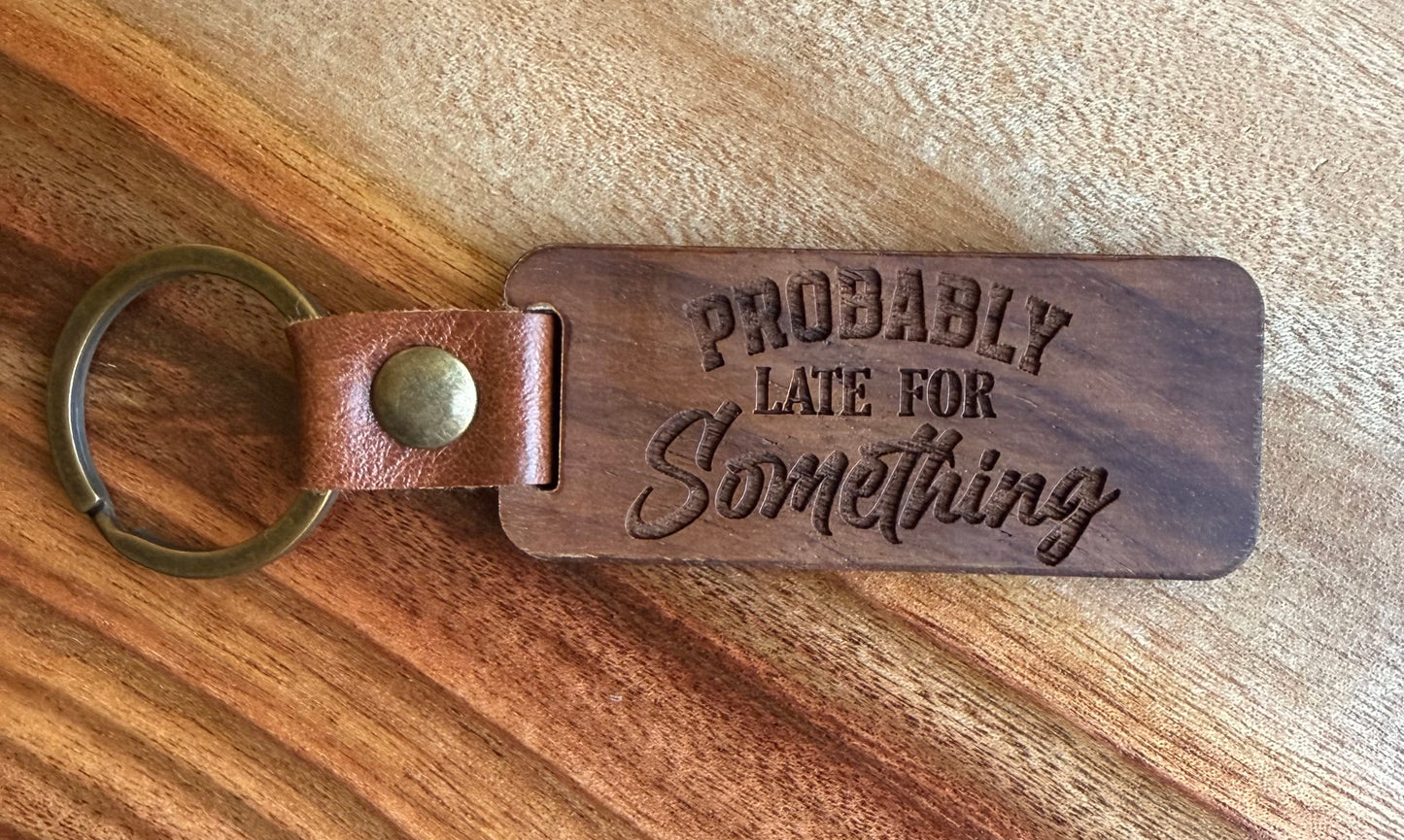 Wooden keychain with 'PROBABLY LATE FOR Something' text on a wooden surface
