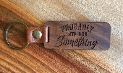 Wooden keychain with 'PROBABLY LATE FOR Something' text on a wooden surface