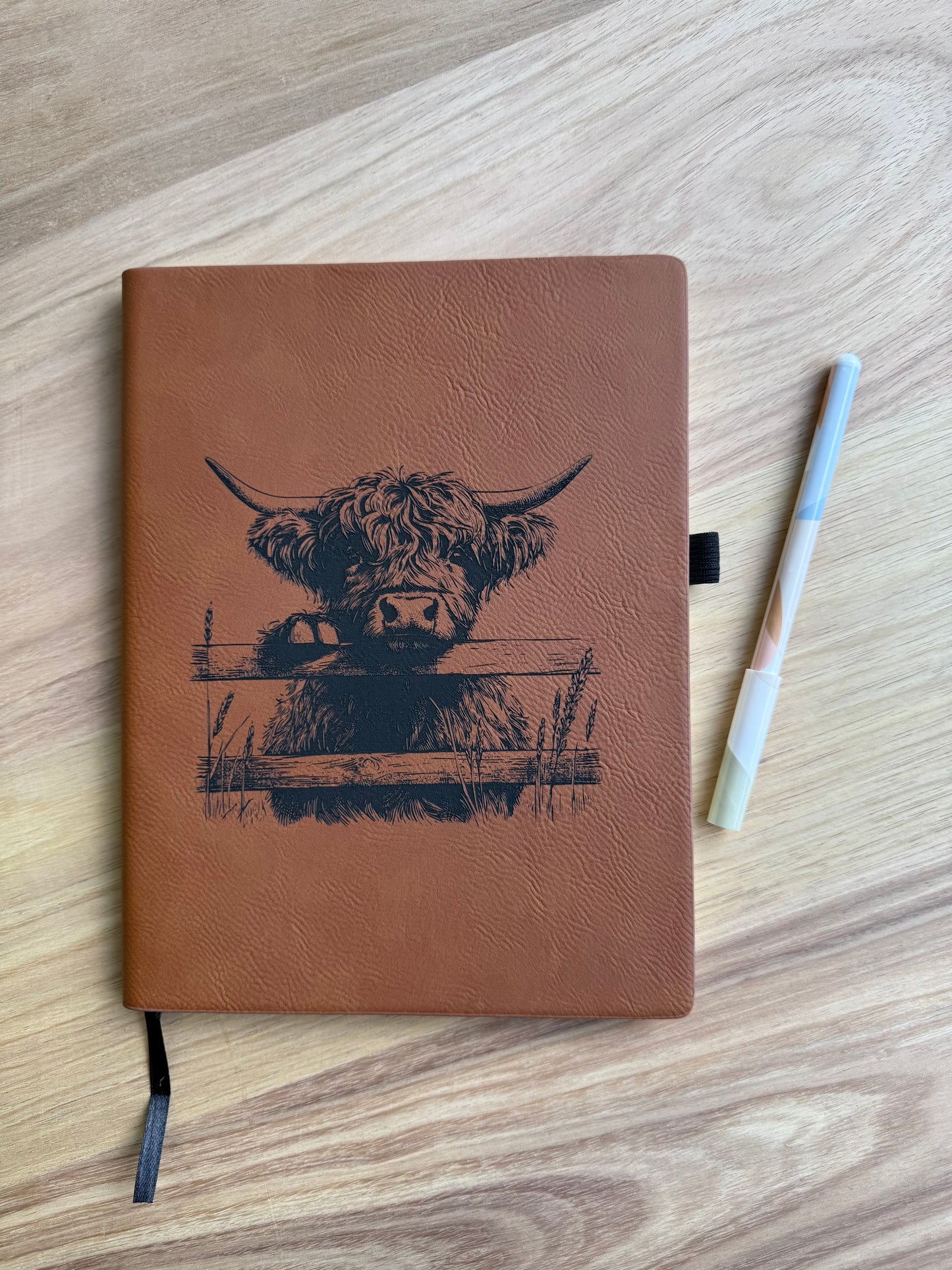 Brown notebook with a highland cow illustration on a wooden surface